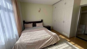 A bedroom with a bed, a nightstand, a wardrobe, and a window with curtains.