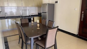 A dining area with a table and chairs, a refrigerator, and a microwave in the background.