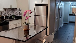 Una cocina moderna con un refrigerador de acero inoxidable, una encimera negra y una orquídea en maceta.