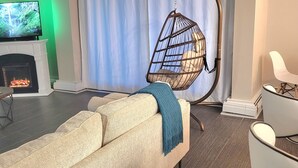 Una sala de estar con sofá, una silla colgante, chimenea y televisor.