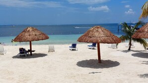 A beach with thatched umbrellas, white lounge chairs, and a clear view of the ocean. - Oceanfront Condo · Hotel Zone · Near Isla Ferry (CancÃºn)