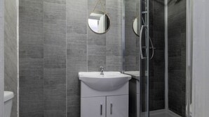 A bathroom with a white sink, a mirror, and a glass shower enclosure. - Elegant Studio: Studio Suite 5 (Coventry)