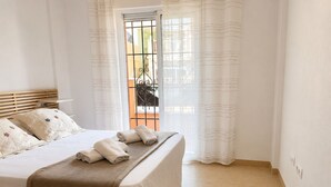 A hotel room with a bed, pillows, a blanket, and a view of a balcony.