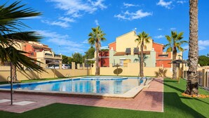 A swimming pool with a clear blue water surface, surrounded by artificial grass and palm trees.
