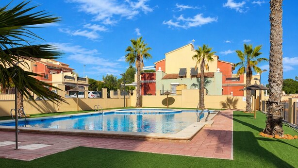 A swimming pool with a clear blue water surface, surrounded by artificial grass and palm trees.