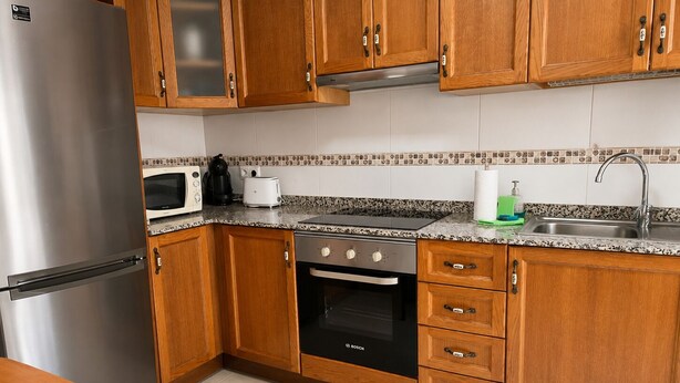 A kitchen with wooden cabinets, a stainless steel refrigerator, a Bosch oven, a microwave, and a sink.