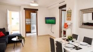 A modern living room with a sofa, a dining table set for four, and a kitchen area with a washing machine.