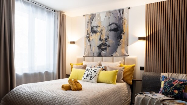 Camera d'albergo con un letto grande, una testiera con un quadro e un comodino con un libro.