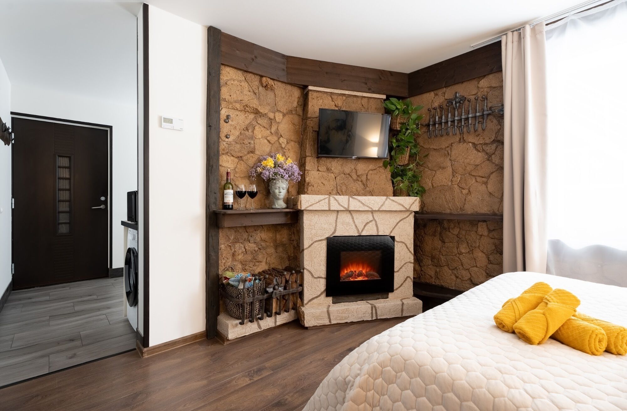 Een slaapkamer met een stenen openhaard, een bed met gele handdoeken, een televisie boven de openhaard en een deur links.