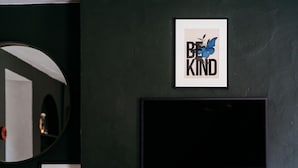 Ein modernes Wohnzimmer mit einer dunkelgrünen Wand, einem Wand-Fernseher, einem hölzernen Bücherregal, einem Kamin mit Holzscheiten und einer Glasvase mit Pflanzen.