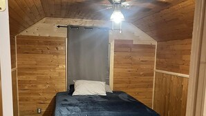 A small, cozy room with a single bed, wooden walls, and a sloped ceiling. - Little cabin near a lake  (Grassland)