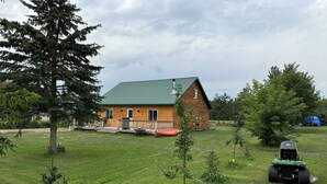 A log cabin with a green roof, surrounded by a grassy yard and trees. - Little cabin near a lake  (Grassland)