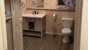 A wooden-paneled bathroom with a sink, toilet, and mirror. - Little cabin near a lake  (Grassland)