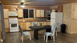 A compact kitchen with wooden cabinets, a microwave, stove, refrigerator, and a dining area with two chairs and a table. - Little cabin near a lake  (Grassland)