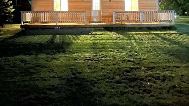 A two-story wooden building with a porch and a fenced yard at night. - Little cabin near a lake  (Grassland)