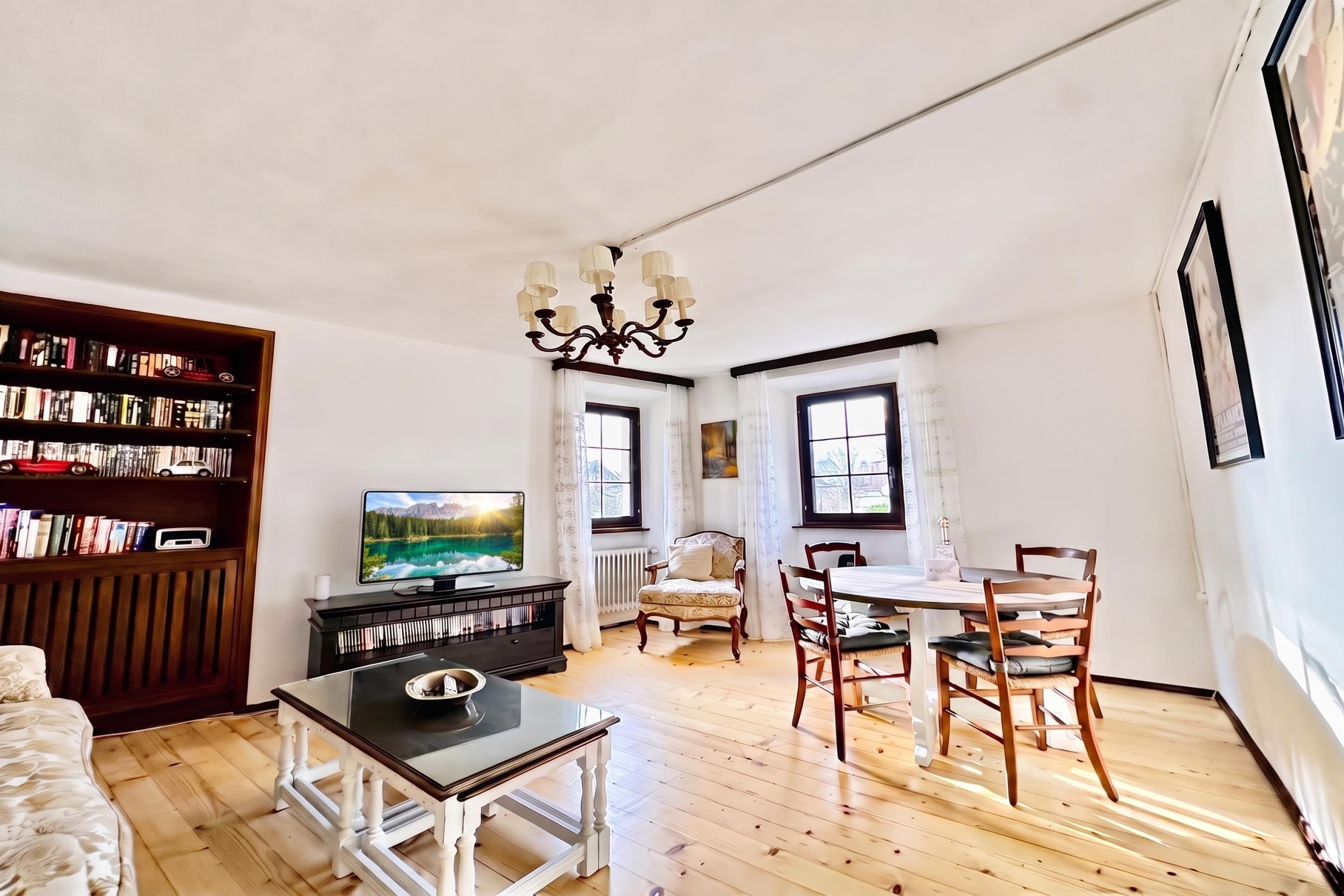 A living room with a television, bookshelves, a dining table with chairs, and a chandelier.