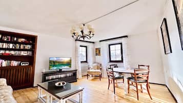 A living room with a television, bookshelves, a dining table with chairs, and a chandelier.
