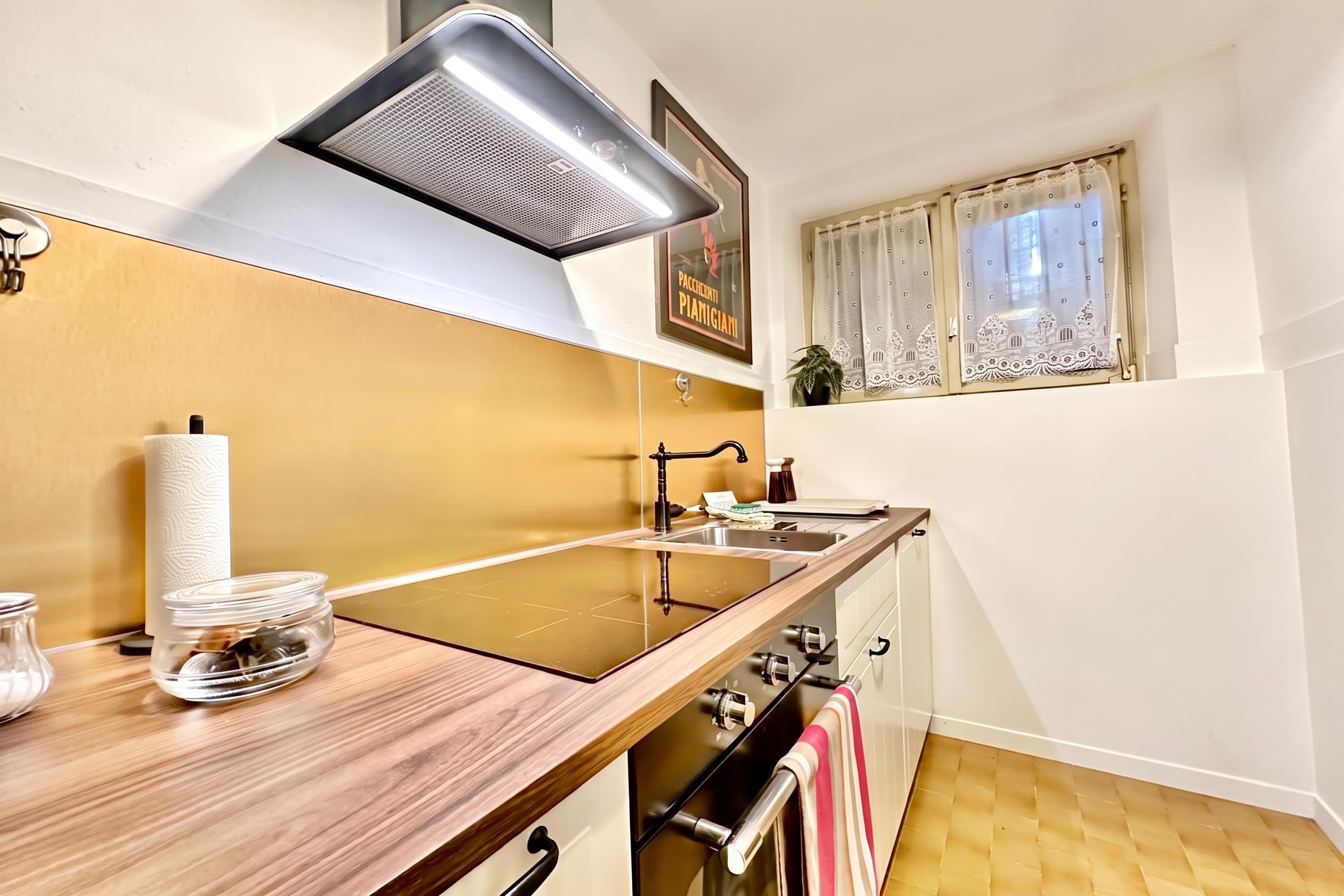 A kitchen with a wooden countertop, a stainless steel sink, a range hood, and a window with lace curtains.