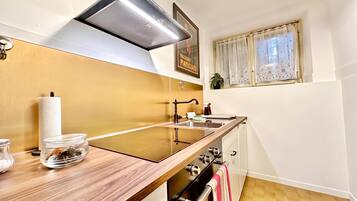 A kitchen with a wooden countertop, a stainless steel sink, a range hood, and a window with lace curtains.