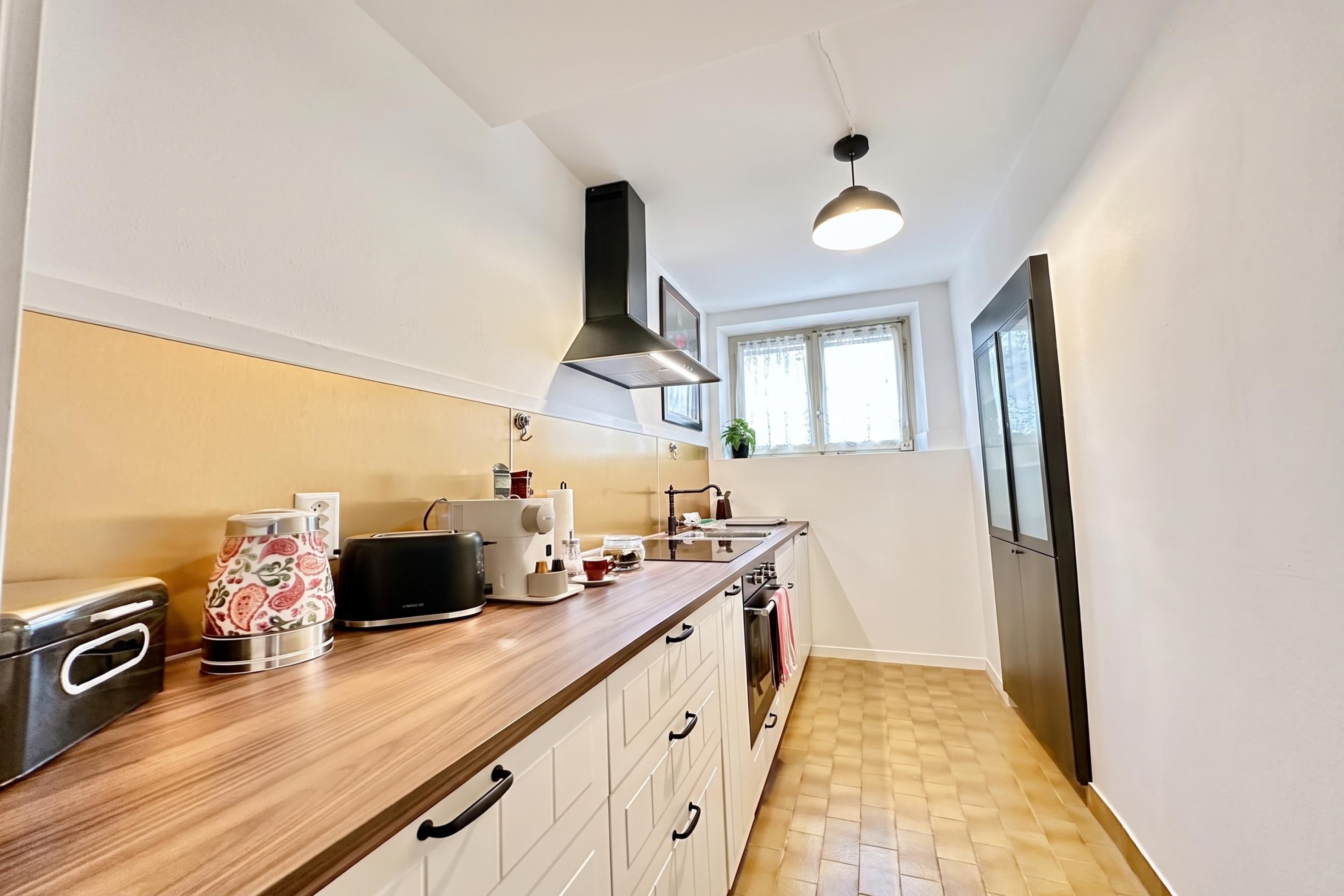 Eine moderne Küche mit Holzarbeitsplatte, Dunstabzugshaube, Einbauofen und einem Fenster mit Vorhängen.
