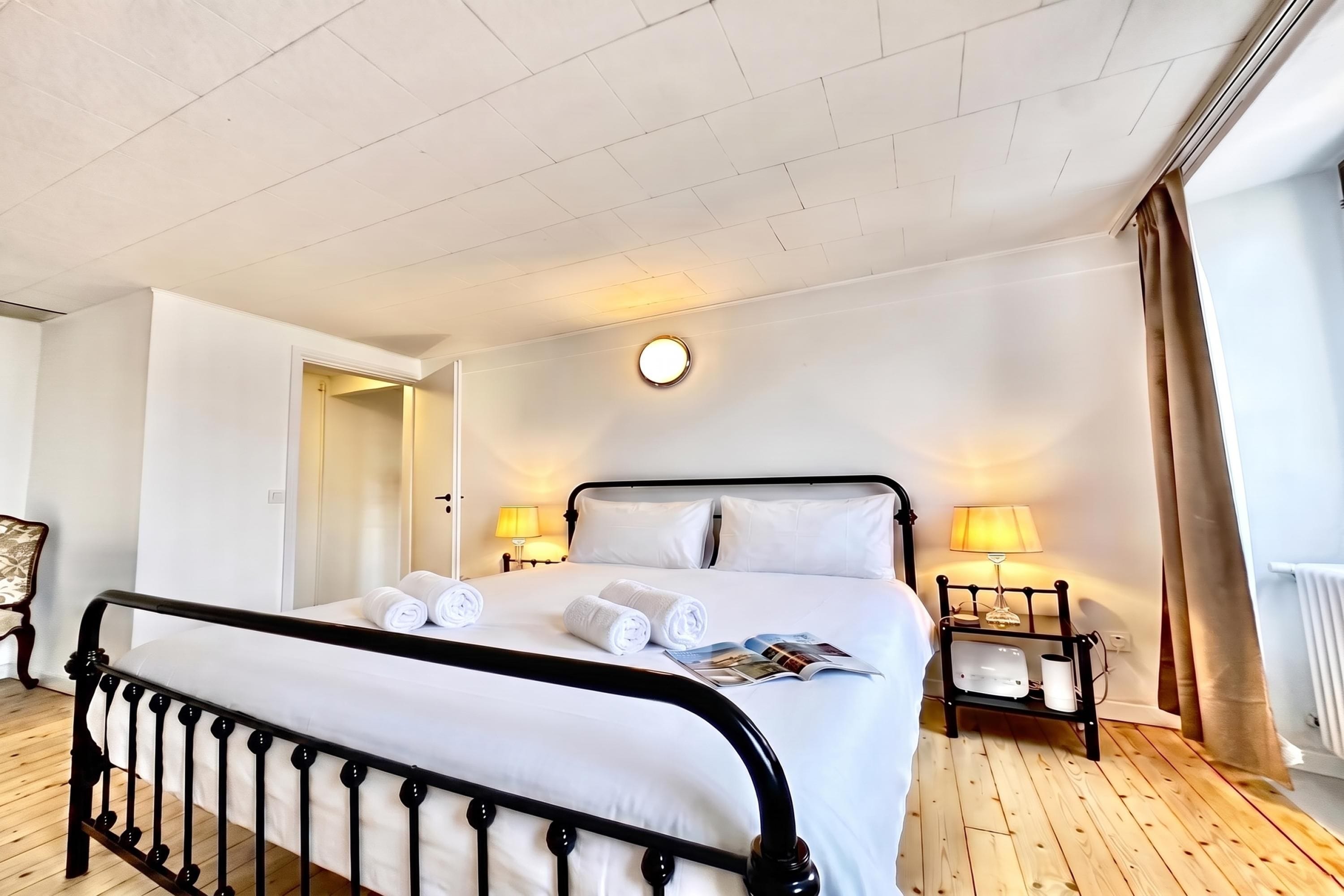 Une chambre d’hôtel avec un lit, deux lampes de chevet, une horloge ronde fixée au mur et un plancher en bois.