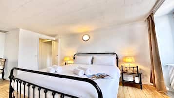 A hotel room with a bed, two bedside lamps, a round wall clock, and a wooden floor.
