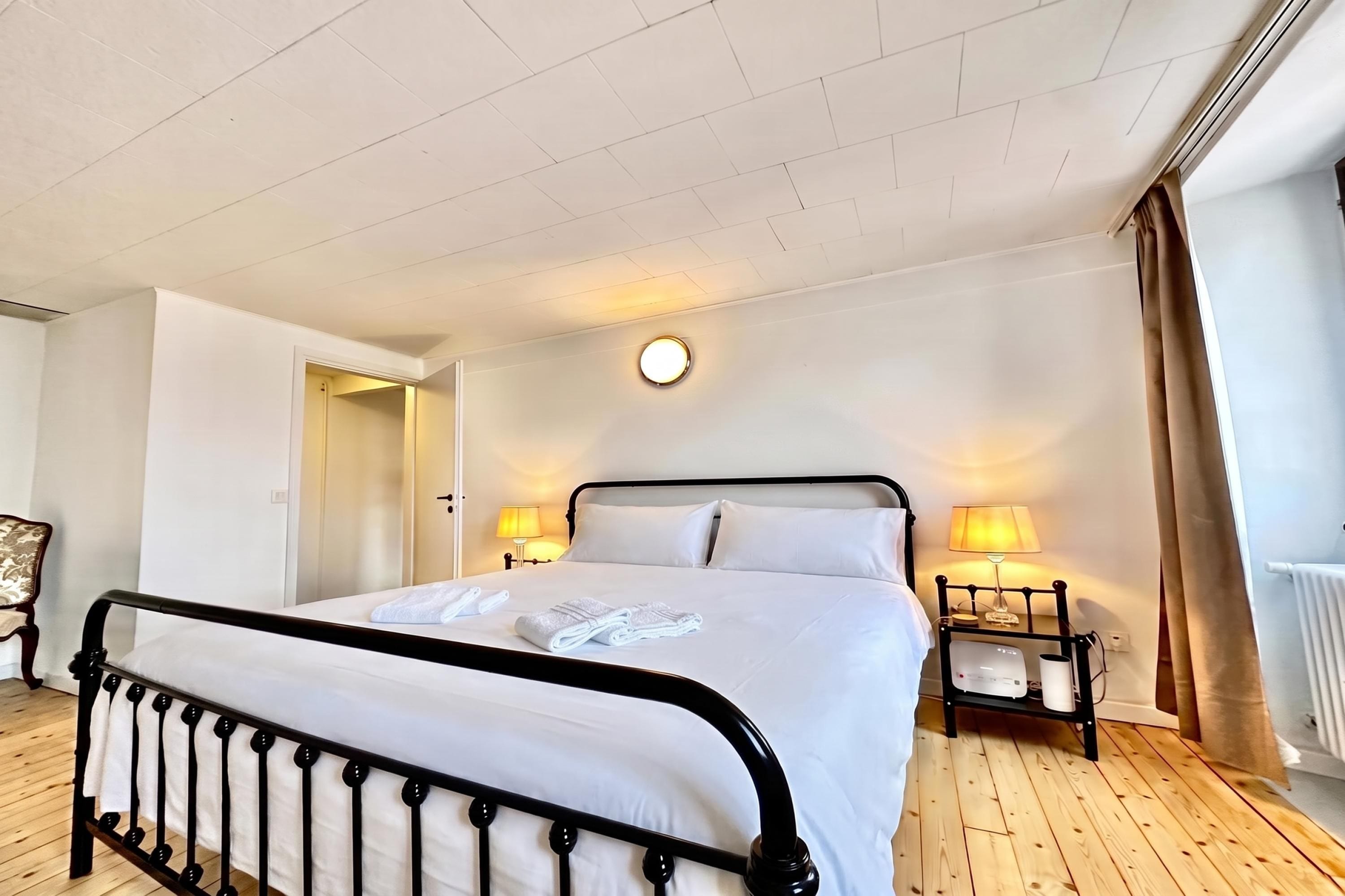 A hotel room with a bed, bedside lamps, a round wall clock, and a wooden floor.