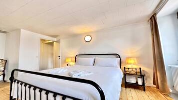 A hotel room with a bed, bedside lamps, a round wall clock, and a wooden floor.