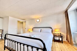 A hotel room with a bed, bedside lamps, a round wall clock, and a wooden floor. - Casa Matilde Apartments (Gambarogno)