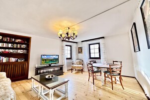 A living room with a television, bookshelves, a dining table with chairs, and a chandelier.