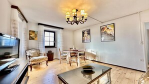 A spacious living room with a wooden floor, a glass coffee table, a chandelier, a dining table with chairs, and a sofa. - Casa Matilde Apartments (Gambarogno)