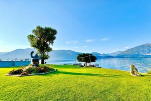 A well-maintained grassy area with a sculpture, a bench, and a clear view of a lake with mountains in the background.