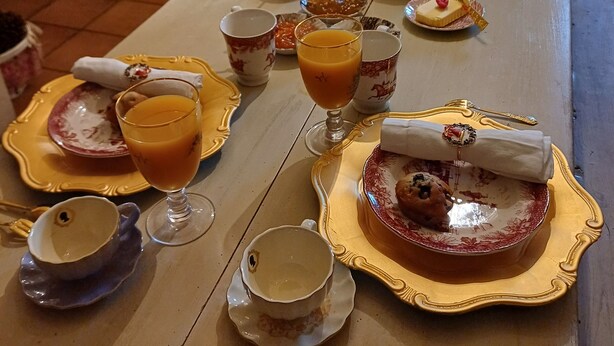 Ein Esstisch ist reichhaltig gedeckt, mit einer Torte, Obst und Getränken. Im Hintergrund sind ein Schrank und Vorhänge zu sehen.