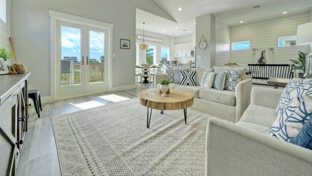 A spacious living room with a large round coffee table, a sofa set, and a dining area visible through glass doors.