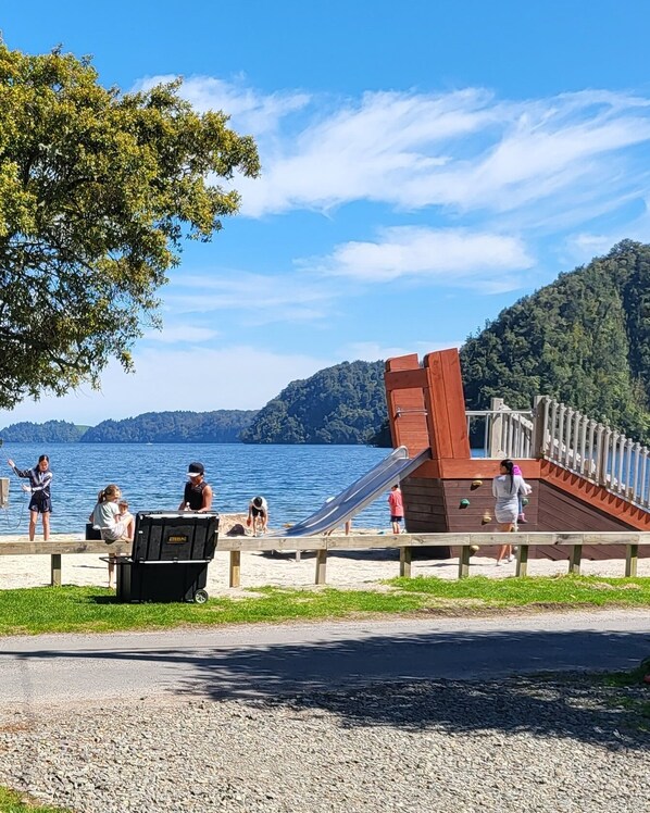 A beachside playground with a slide and a wooden deck overlooking a lake.