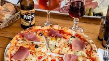 A pizza with various toppings, a bottle of Pietra beer, and a glass of red wine on a wooden table.