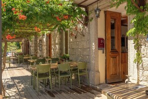 An outdoor dining area with wooden tables and chairs, surrounded by stone walls and covered by a pergola with flowering vines. - AUBERGE U n'Antru Versu (San-Gavino-di-Carbini)