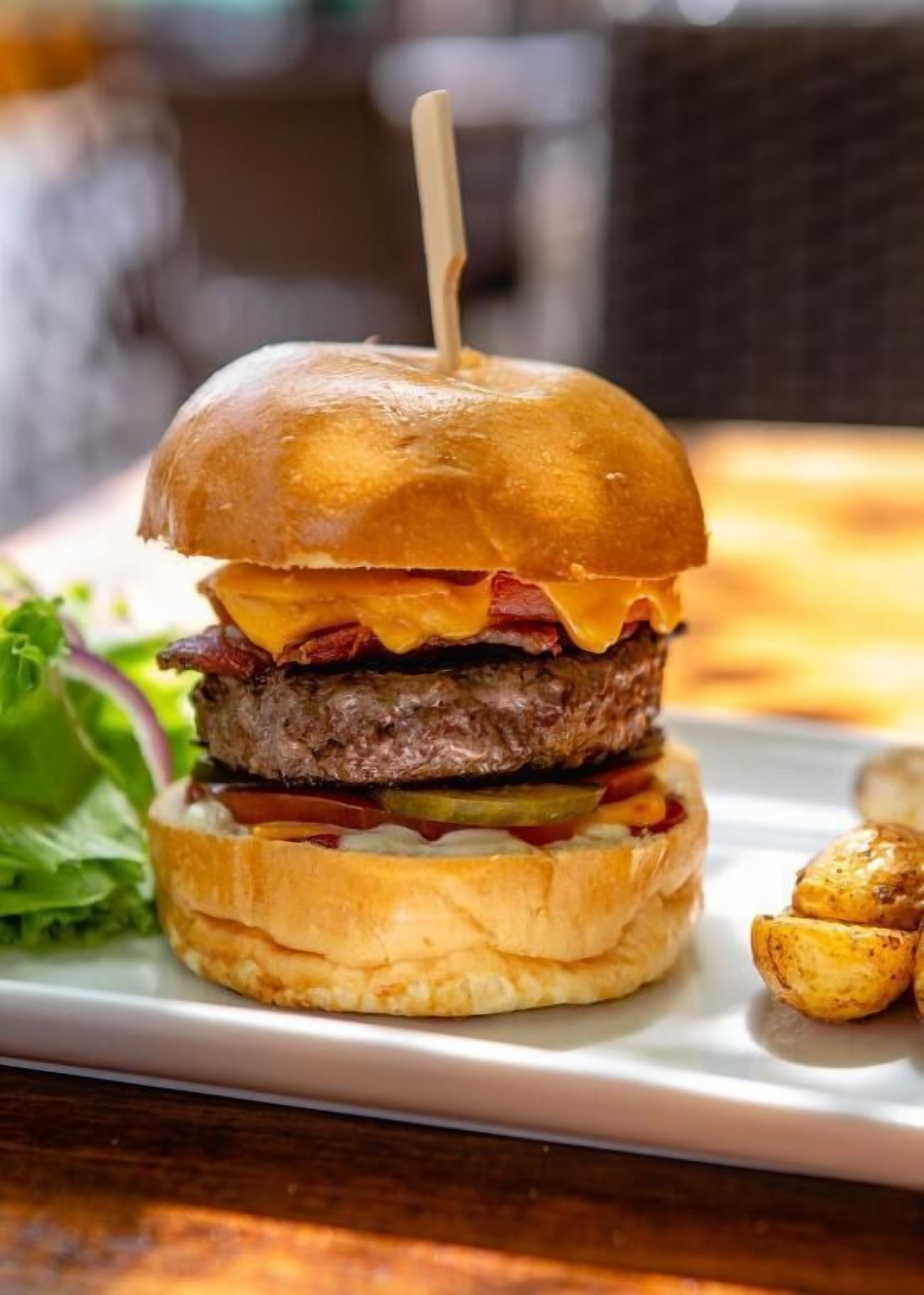 A burger with a toothpick on top, served on a white plate with a side of roasted potatoes.