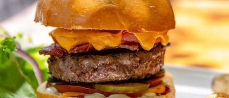 A burger with a toothpick on top, served on a white plate with a side of roasted potatoes.