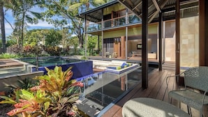 A modern house with a glass-enclosed deck, a pool, and tropical plants.