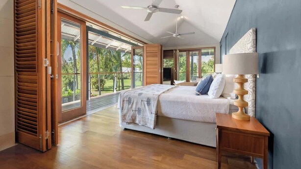 A bedroom with a bed, a nightstand, a ceiling fan, and large windows.