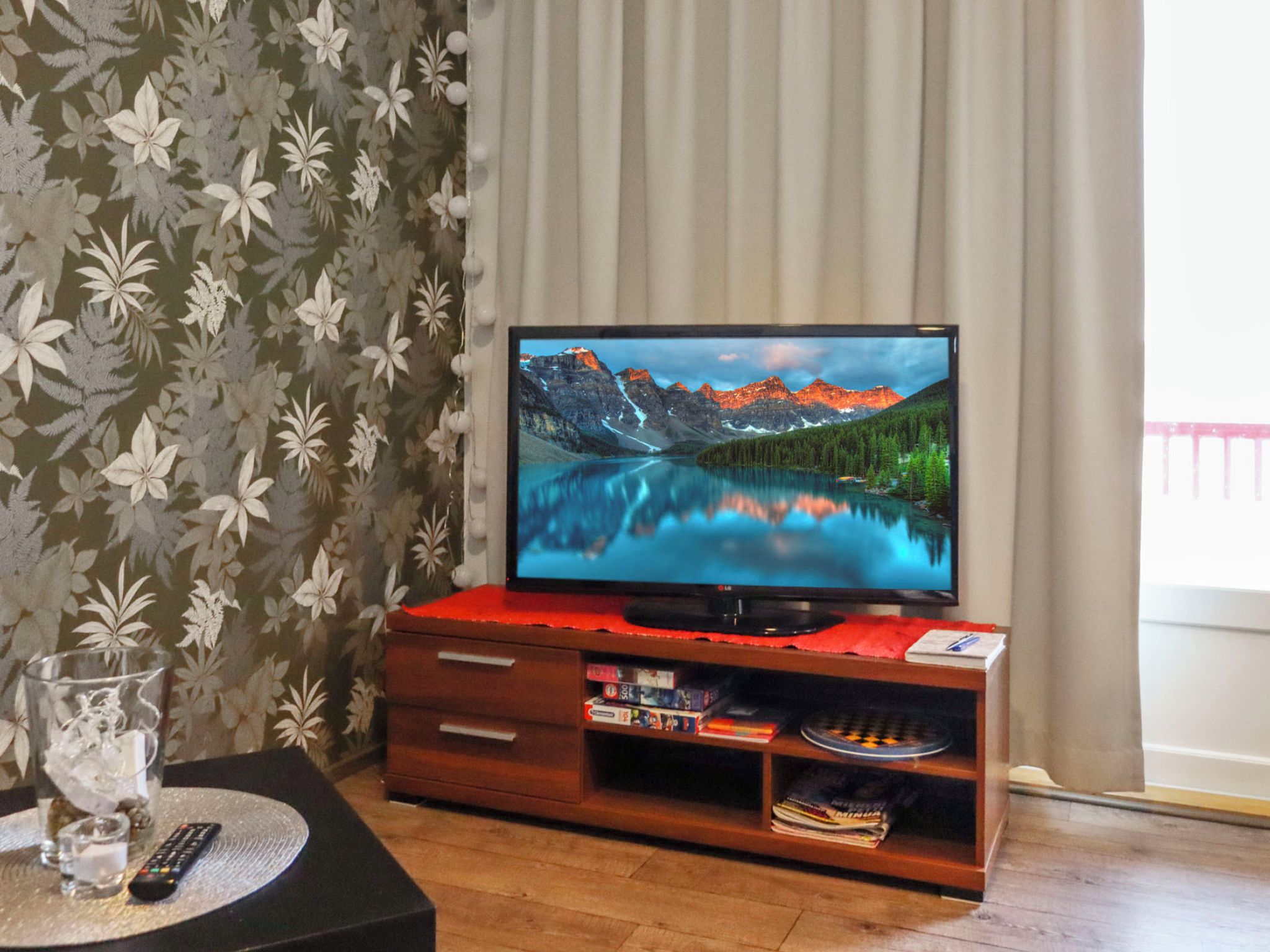 A television on a wooden stand with a remote control, a glass of water, and a book on the stand.