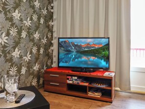 Un téléviseur posé sur un meuble en bois, avec une télécommande, un verre d’eau et un livre sur le meuble.
