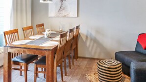 A dining area with a wooden table, chairs, a pendant light, and a painting on the wall.