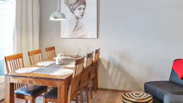 A dining area with a wooden table, chairs, a hanging pendant light, and a painting on the wall.