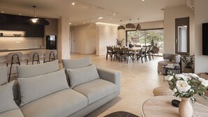 A modern living room with a grey sofa, dining area with a table and chairs, and a kitchen in the background. - Villa Agali Free* heated pool & 70m to Sea! (Chania)