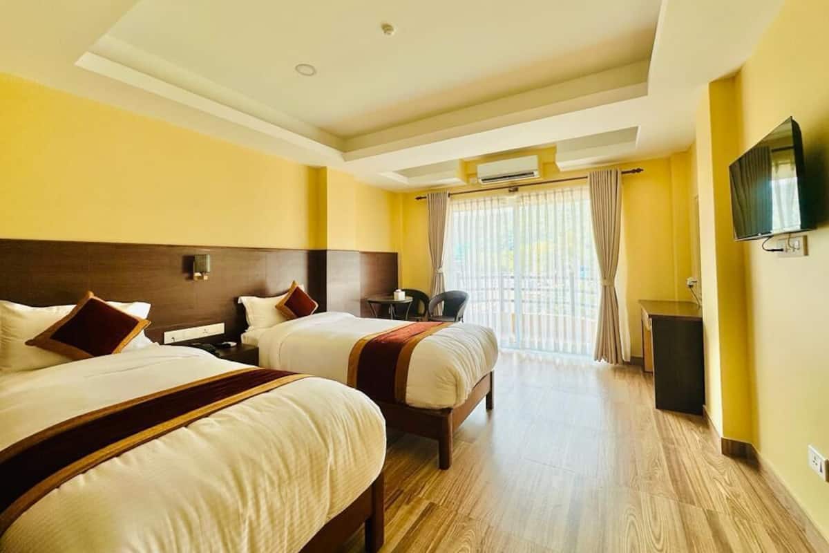 A hotel room with two beds, a television, an air conditioning unit, and a window with curtains.