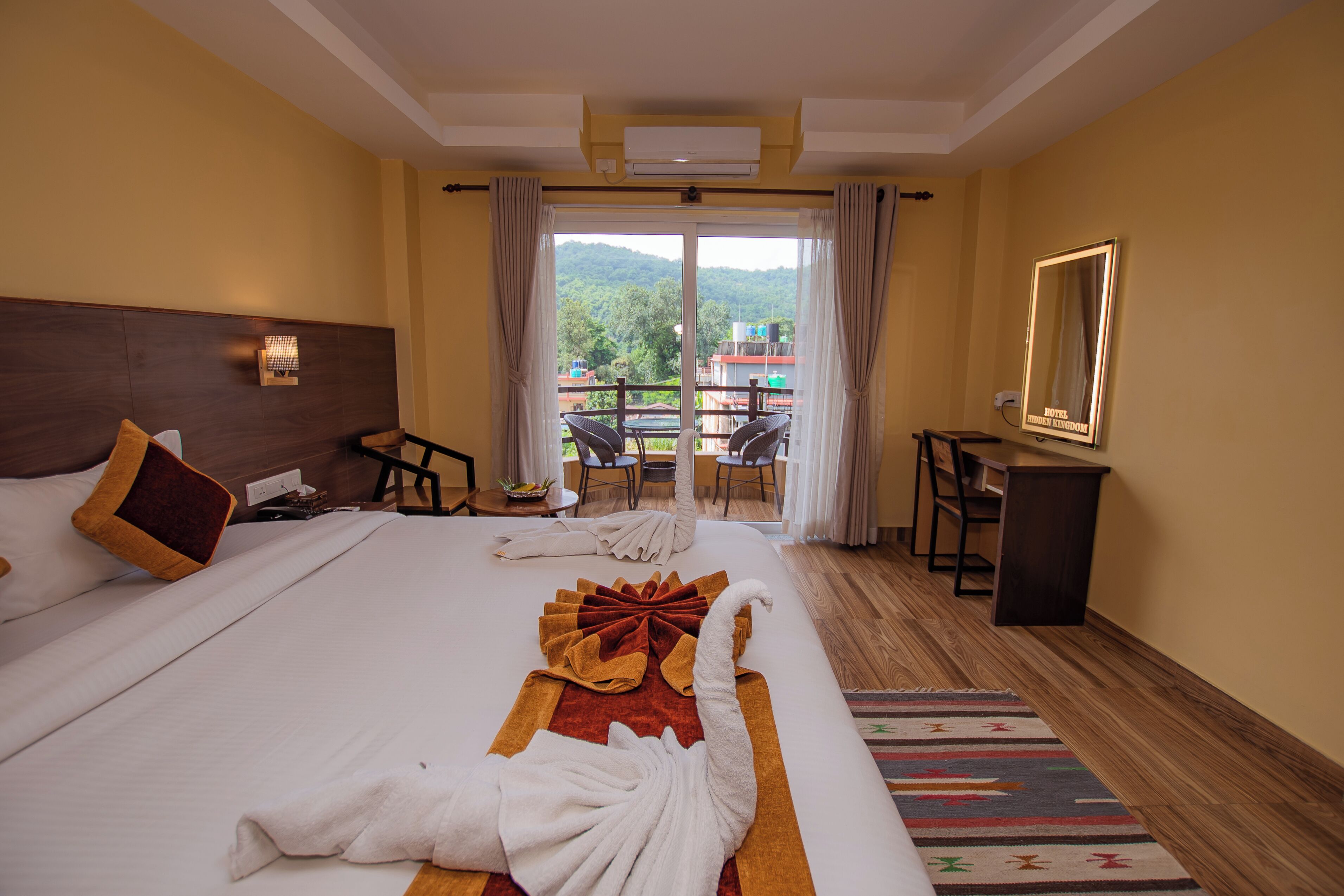 Habitación de hotel con una cama grande, un escritorio, una silla y un balcón con vistas a zonas verdes.