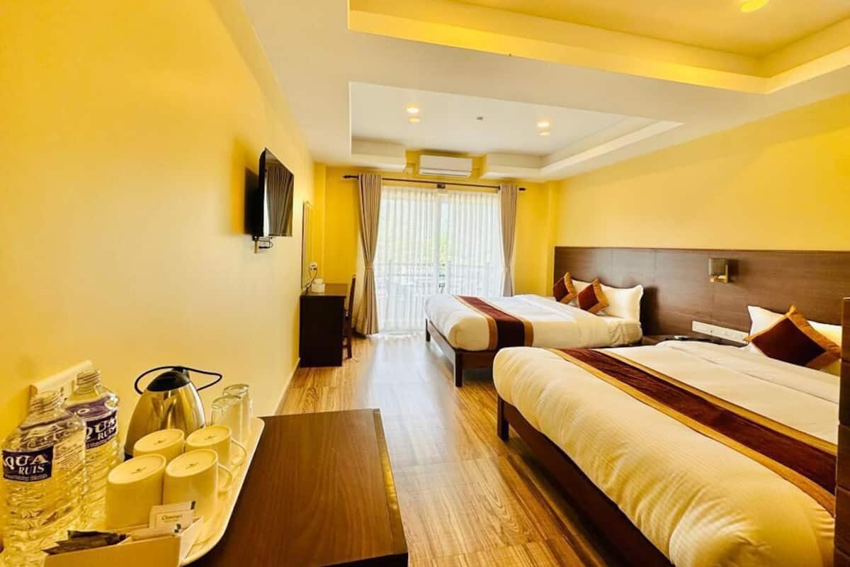 A hotel room with two beds, a wooden floor, a flat-screen TV, and a tray with toiletries.