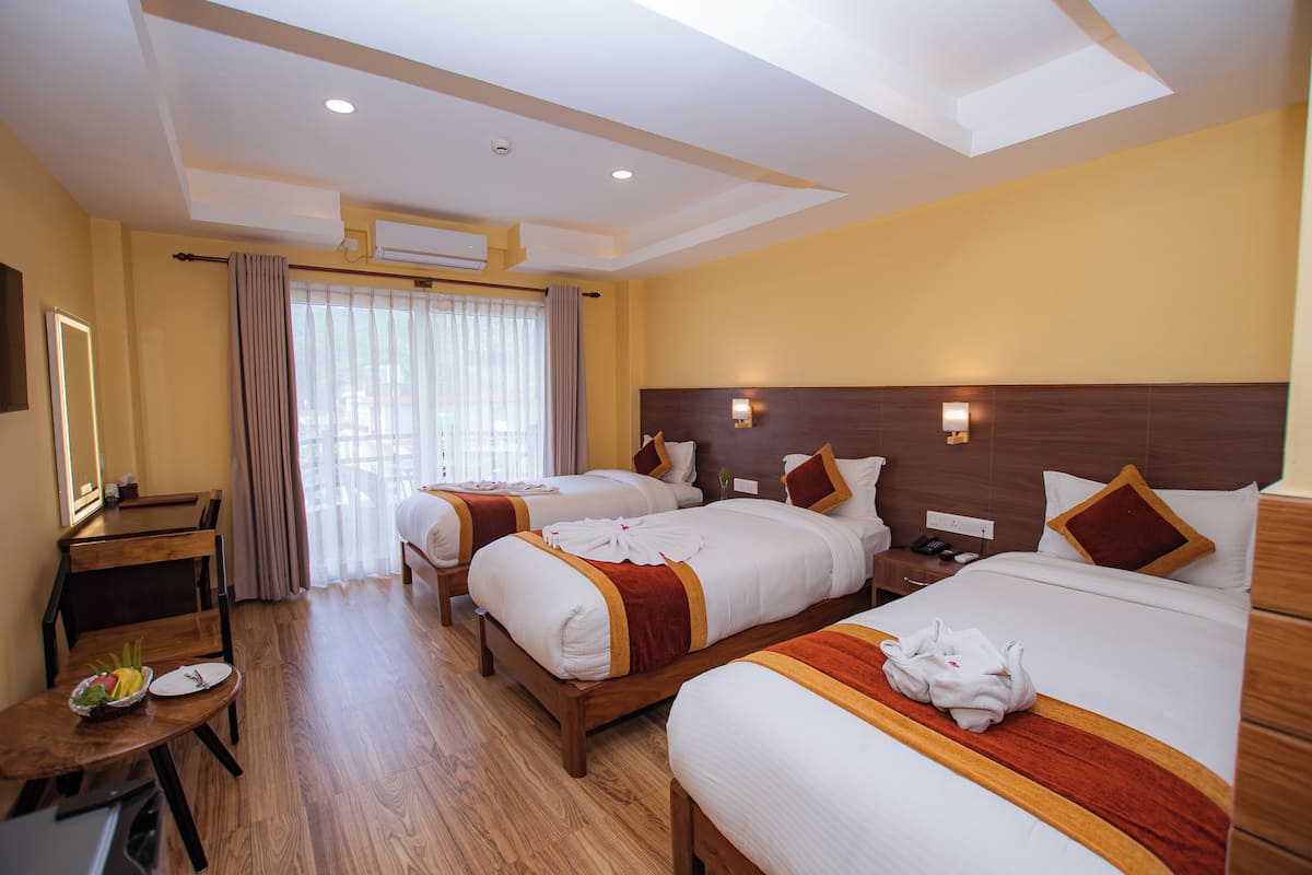 A hotel room with two beds, a desk with a chair, a small table with a fruit bowl, and a window with curtains.